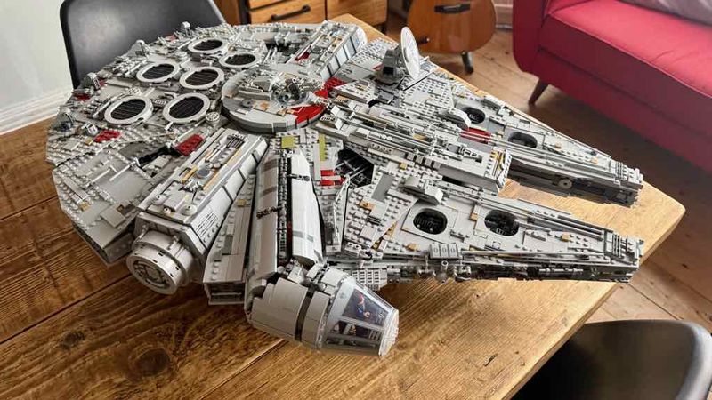 The LEGO Millennium Falcon with the round radar dish, on a rustic wooden table; Han Solo and Chewbacca are in the cockpit.