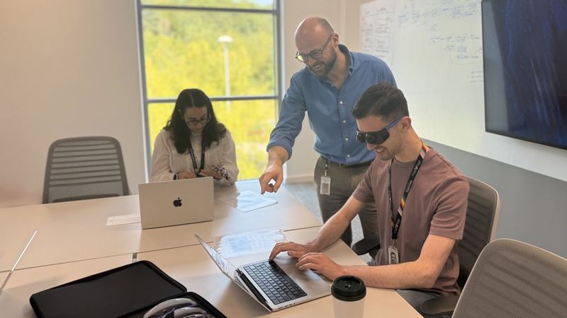 Martin Underhill directing a small accessibility empathy lab, working with a man who has visual impairment goggles on, while a woman next to them puts on motor impairment gloves.